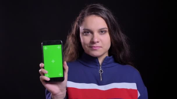 Primo piano ritratto di adulto attraente femmina caucasica che mostra il telefono con schermo verde alla fotocamera con sfondo isolato su nero — Video Stock