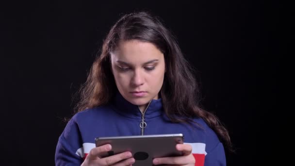 Retrato de primer plano de la atractiva hembra caucásica adulta escribiendo en la tableta con fondo aislado en negro — Vídeos de Stock