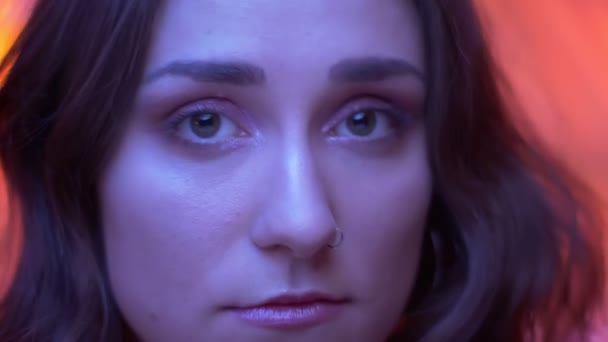 Съемки крупным планом молодого привлекательного кавказского женского лица с красивыми глазами, смотрящими в камеру на неоновом красном фоне — стоковое видео