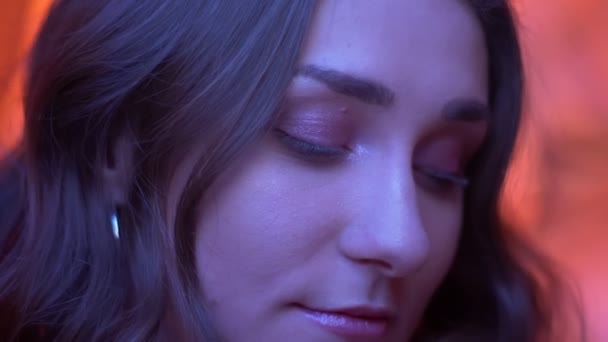 Nahaufnahme eines jungen attraktiven kaukasischen weiblichen Gesichts, das mit lächelndem Gesichtsausdruck vor neonrotem Hintergrund in die Kamera blickt — Stockvideo