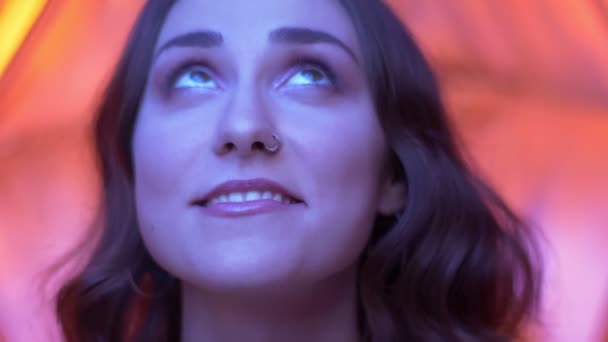 Съемка крупным планом молодого привлекательного кавказского женского лица с красивыми глазами, смотрящего в камеру на неоновом красном фоне — стоковое видео