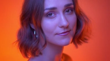 Genç çekici beyaz kadın kamera dönüm ve Neon kırmızı arka plan ile neşeli gülümseyen closeup çekim