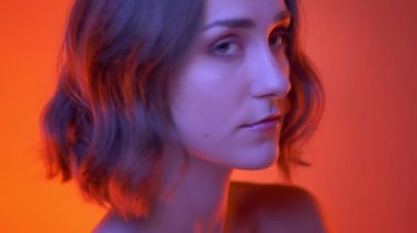 Neon kırmızı arka plan ile kamera bakarak burun piercing ile genç çekici beyaz kadın closeup yan görünüm çekimi