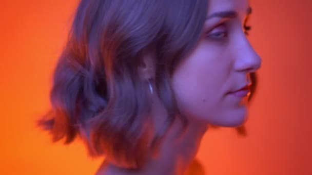 Close-up schieten van jonge aantrekkelijke Kaukasische vrouwelijke draaien om de camera en glimlachend gelukkig met neon rode achtergrond — Stockvideo