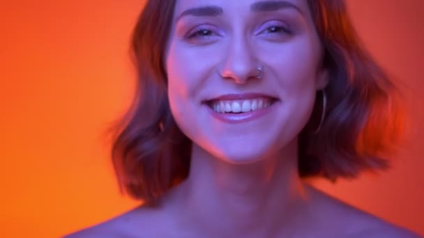 Крупним планом знімок молодої привабливої білої жінки, дивлячись на камеру, що сміється з радості з неоновим червоним фоном — стокове відео