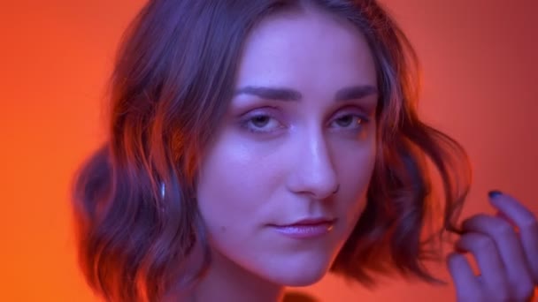 Closeup shoot of young attractive caucasian female being sexy playing with her hair looking at camera with neon red background — Stock Video