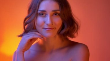 Çıplak omuzları ile genç çekici beyaz kadın closeup ateş baştan çıkarıcı Neon kırmızı arka plan ile kamera bakarak gülümseyen