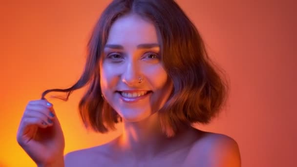 Съемки крупным планом молодой привлекательной белой женщины с обнаженными плечами, смотрящей в камеру на неоновом красном фоне — стоковое видео
