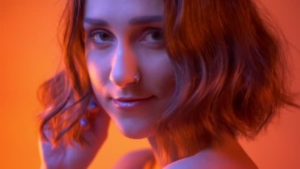 Close-up schieten van jonge vrolijke Kaukasische meisje met mooie make-up glimlachen en draaien om de camera met neon rode achtergrond — Stockvideo