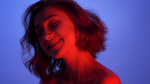 Closeup shoot of young attractive caucasian female smiling seductively looking at camera with neon blue and red background — Stock Video