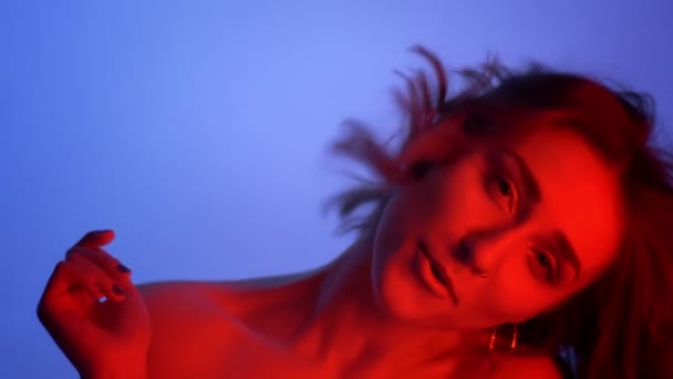 Closeup shoot of young gentle caucasian female smiling and tossing her hairlooking at camera with neon blue and red background — Stock Video