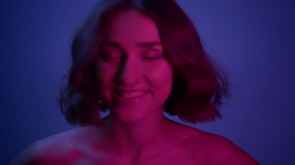 Close-up tiro de jovem sexy fêmea sorrindo feliz olhando para a câmera com seu cabelo tremulando com neon azul fundo — Vídeo de Stock