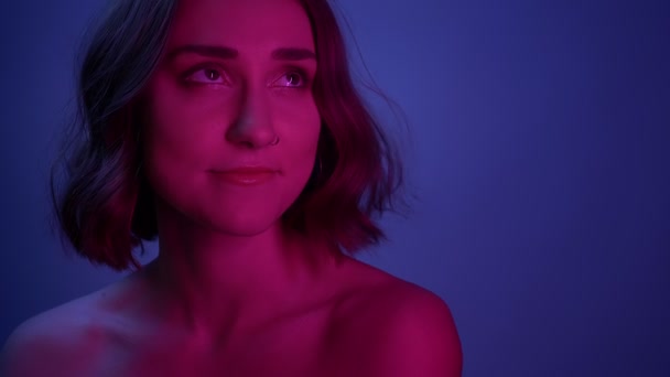 Closeup shoot of young sexy female smiling looking at camera with her hair fluttering with neon blue background — Stock Video