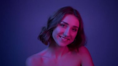 Neon mavi arka plan ile saç çırpınan ile kameranın önünde poz gülümseyen genç seksi kadın closeup çekim