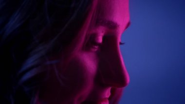 Neon mavi arka plan ile kameranın önünde mutlu gülümseyen genç güzel kadın yüzü closeup yan görünüm çekimi