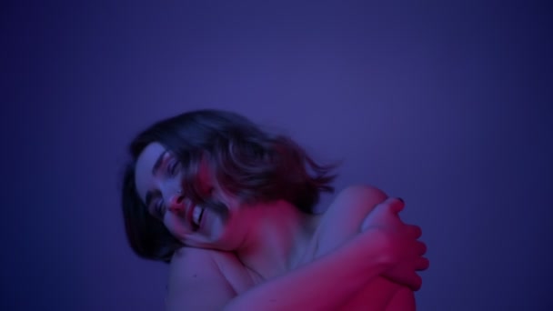 Съемки крупным планом молодой милой женщины, улыбающейся и обнимающейся перед камерой на неоновом синем фоне — стоковое видео
