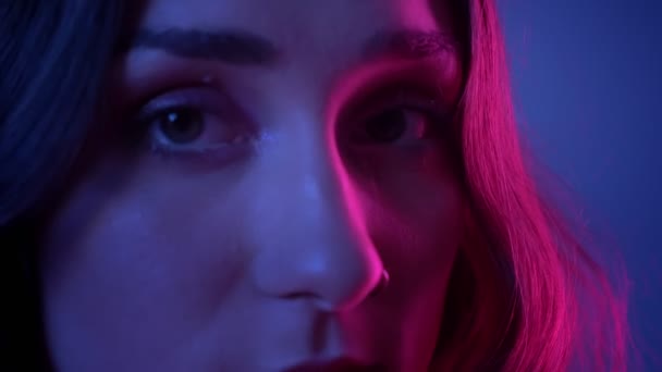 Close-up zijaanzicht schieten van jonge mooie vrouwelijke gezicht draaien om de camera met neon blauwe achtergrond — Stockvideo