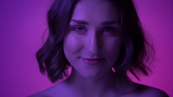 Neon mavi arka plan ile kameranın önünde neşeli gülüyor genç güzel kız closeup ateş — Stok video