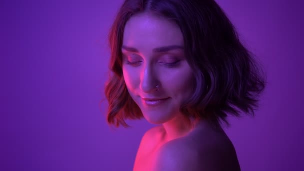 Closeup side view shoot of young alluring female posing in in front of the camera with neon purple background — Stock Video