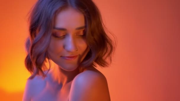 Closeup shoot of young attractive caucasian female with naked shoulders seductively looking at camera with neon red background — Stock Video