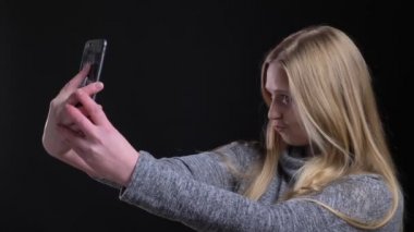 Siyah arka plan üzerinde akıllı telefon üzerinde flört selfie-fotoğraf yapma sarışın düz saçlı kız portre.