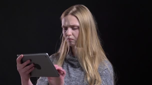 Porträtt av ung blond Straight-haired modell tittar i tablett med nöje på svart bakgrund. — Stockvideo