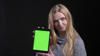 Siyah arka planda uygulamayı tavsiye etmek için sevinçle tablet yeşil ekran gösteren sarışın düz saçlı uzman portresi.