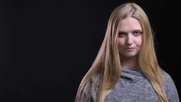 Portrait of young blonde straight-haired expert watching seriously and intently into camera on black background. — Stock Video