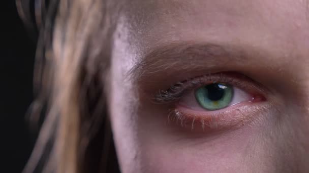 Close-up Eye-portret van jonge blonde vrouw kijken bescheiden in de camera op zwarte achtergrond. — Stockvideo