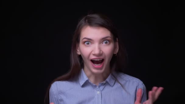 Porträt einer jungen brünetten Geschäftsfrau in blauer Bluse, die vor schwarzem Hintergrund fröhliche Belustigung in die Kamera zeigt. — Stockvideo