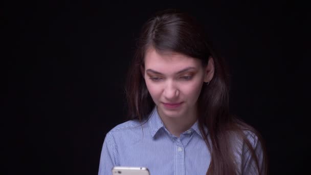Ładna Brunetka biznesmen w niebieskiej bluzce pracując z radością ze smartfonem zamienia się w kamerę i uśmiechy na czarnym tle. — Wideo stockowe