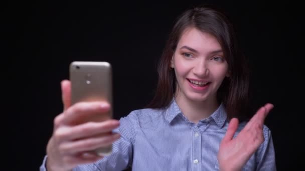 Blijde brunette zakenvrouw in blauwe blousehaving videocall op smartphone Wave hand om een persoon te begroeten op zwarte achtergrond. — Stockvideo