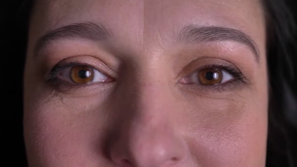 Close-up eye-portrait of middle-aged woman watching with extremely happy smile into camera on black background. — Stock Video