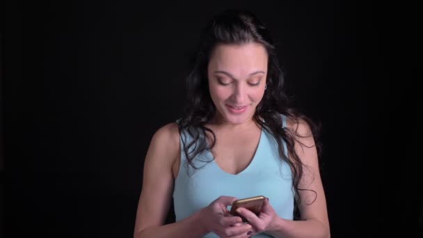 Retrato de mujer de mediana edad mirando con agradable interés en el teléfono inteligente sobre fondo negro . — Vídeos de Stock