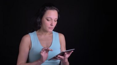 Tablet içine ciddi ilgi ile izlerken Orta yaşlı kadın portre ve siyah arka planda kamera bakıyor.