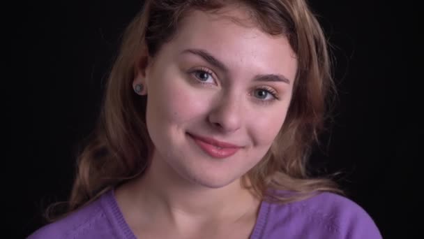 Close-up portrait of cute woman smiling into camera happily on black background. — Stock Video