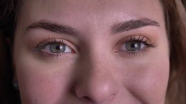 Güzel sarışın kadın gülümseyerek itekler ve siyah arka planda kamera içine izlerken yakın çekim göz-portre.