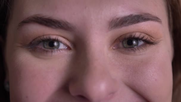 Close-up Eye-portret van mooie blonde vrouw kijken glimlachend in de camera en knippert op zwarte achtergrond. — Stockvideo