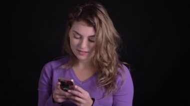 Mutlu kadın portre siyah arka plan üzerinde akıllı telefon içine tür gülümseme ile izliyor.