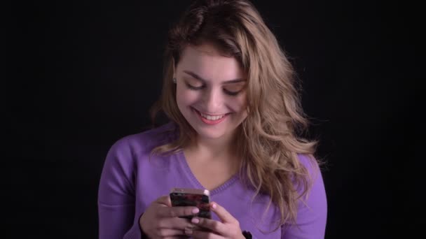 Mutlu kadın portre siyah arka planda tür gülümseme ile kamera içine akıllı telefon saatleri ile çalışan. — Stok video