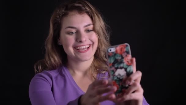 Portrait of joyful blonde woman having a video call on smartphone on black background. — Stock Video