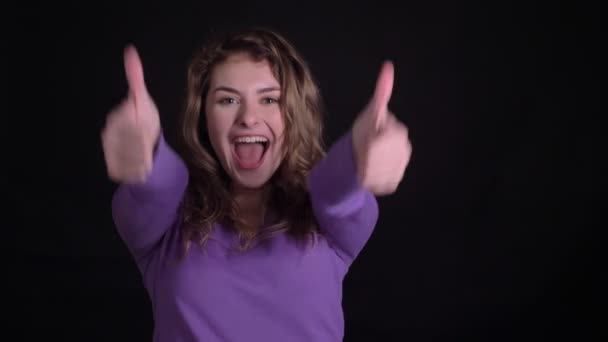 Portrait of cute woman gesturing finger-up signs joyfully into camera to show like and respect on black background. — ストック動画