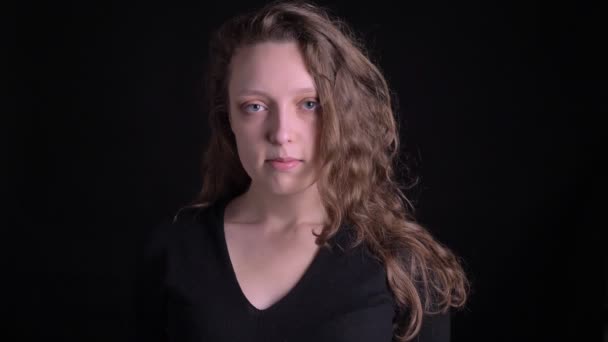 Portrait of young curly-haired girl watching awkwardly into camera on black background. — Stock Video