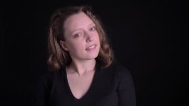 Siyah arka planda kameraya flört gülümseme ile izlerken mütevazı genç kıvırcık saçlı kız portre.