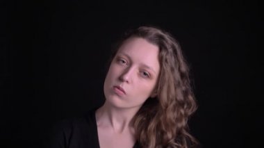 Portrait of young curly-haired girl posing seriously and flirtingly into camera on black background.