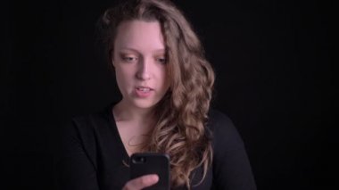 Siyah arka plan üzerinde Smartphone kullanarak videochat sevinçle konuşan genç kıvırcık saçlı kız portre.