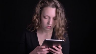 Tablet içine ciddiye izlerken ve siyah arka planda kameraya gülümsüyor dahil genç kıvırcık saçlı kız portresi.