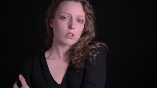 Portrait de jeune fille aux cheveux bouclés posant à la mode dans la caméra et sérieusement sur fond noir . — Video