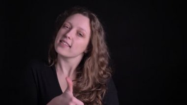 Siyah arka planda kamera içine gizemli gülümseme gibi ve saygı gösteren parmak-up genç kıvırcık saçlı kız.