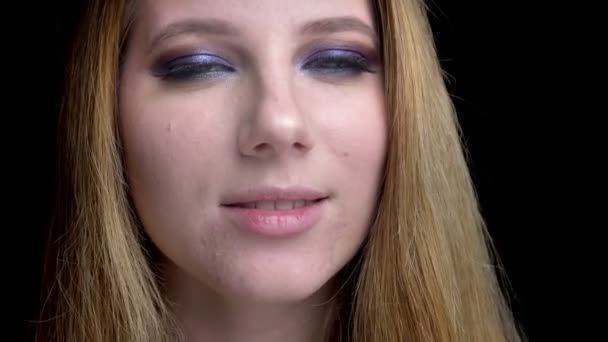 Close-up tiro de jovem bela cara feminina sedutoramente olhando para a câmera com maquiagem deslumbrante com fundo isolado em preto — Vídeo de Stock